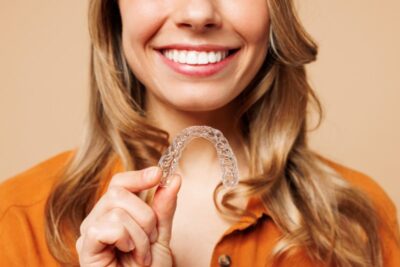 A woman holding a clear Invisalign aligner.
