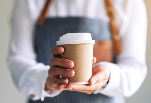 Barista holding out a travel cup for hot coffee.