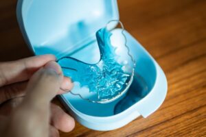 Hand holding retainer perched above its case.